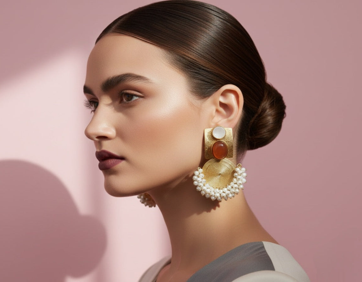 Woman wearing gold and red earrings with a pink background