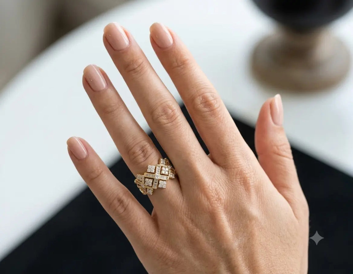 Hand wearing a gold ring with diamond design on a blurred background