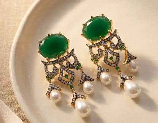 Pair of earrings with green gemstones and pearl accents on a beige plate.